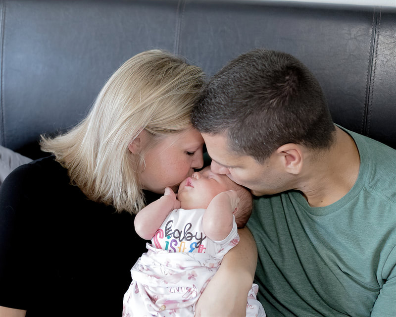 Mom and dad on bed kissing newborn baby on top of head, lifestyle newborn photography, Lakewood Ranch, Florida