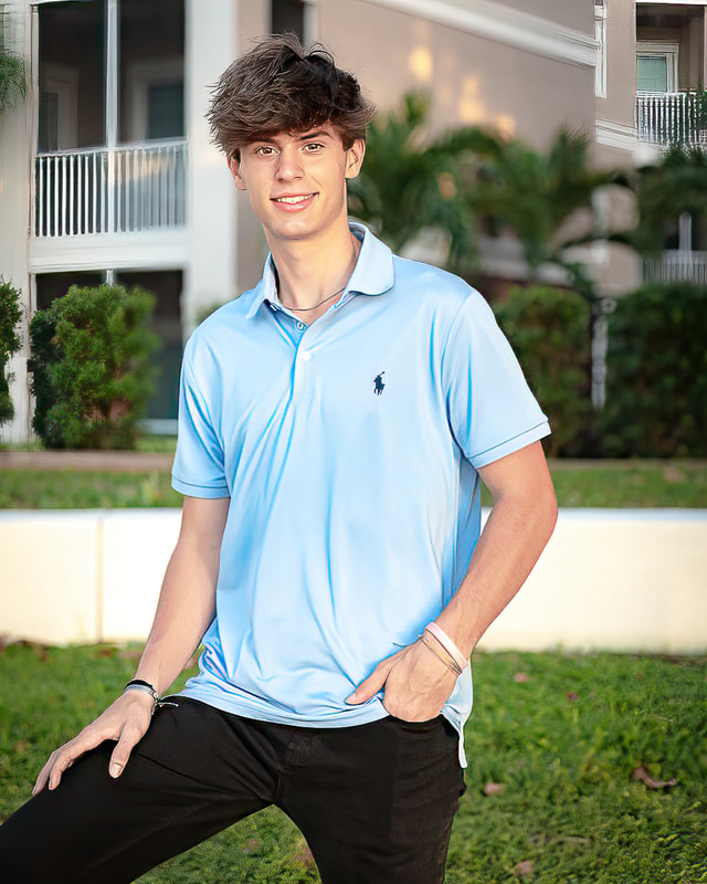 High-school-senior-guy-standing-with-one-leg-propped-up-with-hand-on-leg-other-hand-in-pocket-Bradenton-Riverwalk