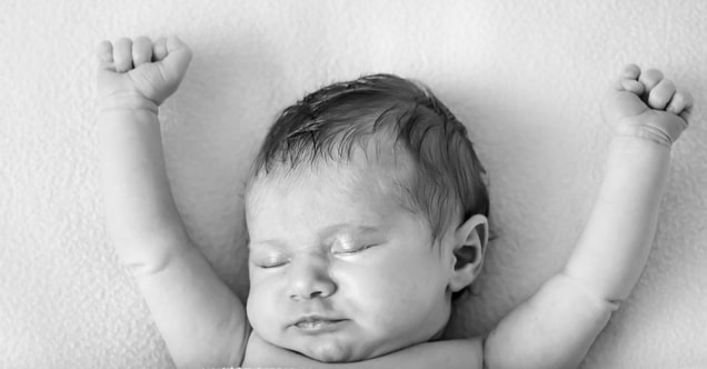 Black and white baby on back with hands stretched above head