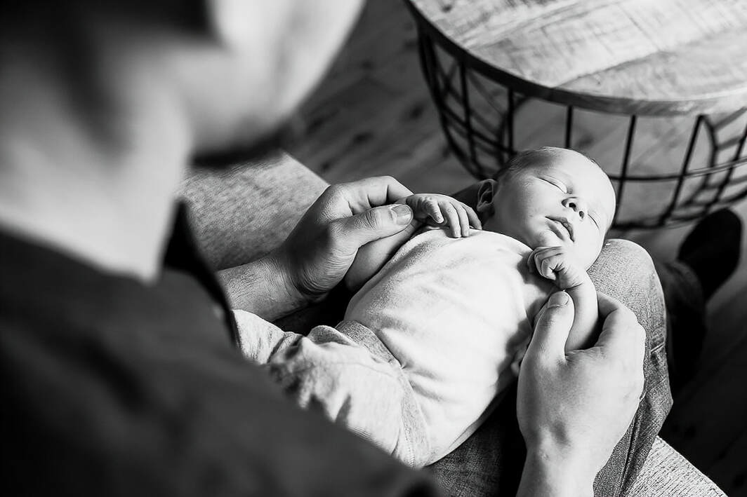 Black and white, dad holding newborn baby on lap, in-home lifestyle newborn photography