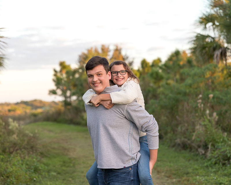 Older brother holding younger sister on back, golden hour, Celery Fields, Sarasota, Florida