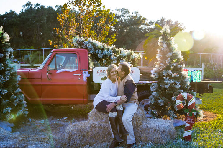 Man kissing side of woman's face with Christmas decorated truck